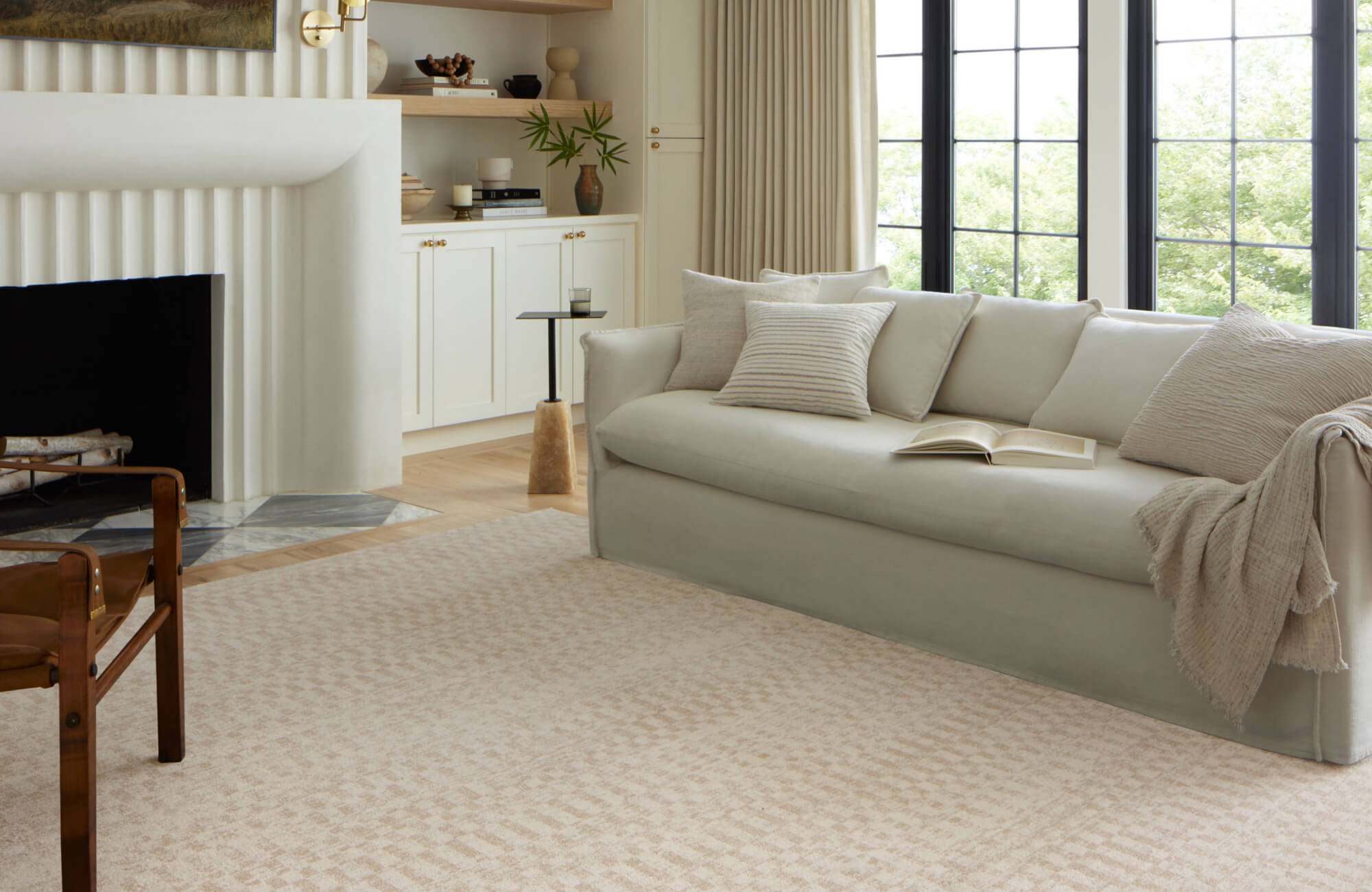 Polyester rug in a soft beige pattern anchoring a neutral living room with a curved cream sofa, light wood accents, and a sculptural fireplace.