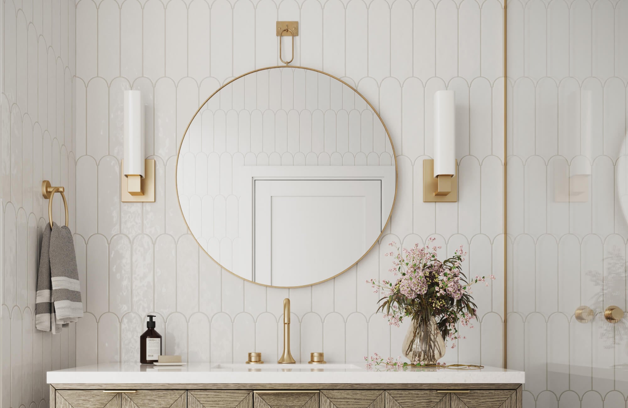 null Refined bathroom with white scalloped tiles, brass-accented sconces, a round mirror, and a floral arrangement on the vanity.