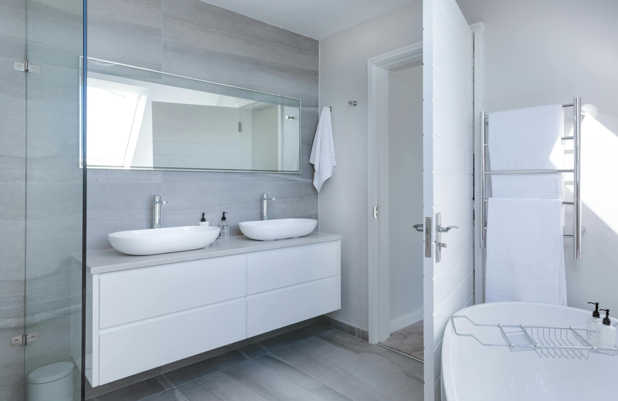 null Minimalist bathroom with light gray tiles, large rectangular mirror, floating vanity with vessel sinks, and chrome towel warmer.