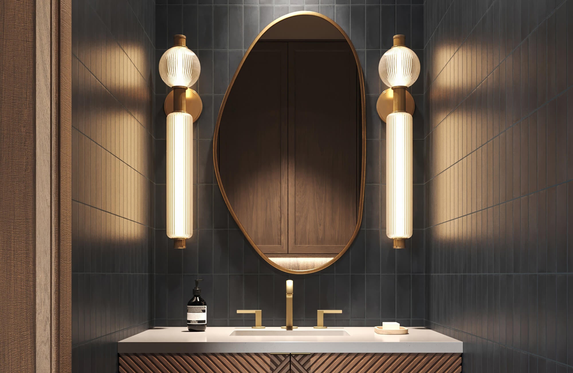 null Moody bathroom with deep navy vertical tiles, sculptural fluted sconces, an asymmetrical mirror, and brass-accented vanity.