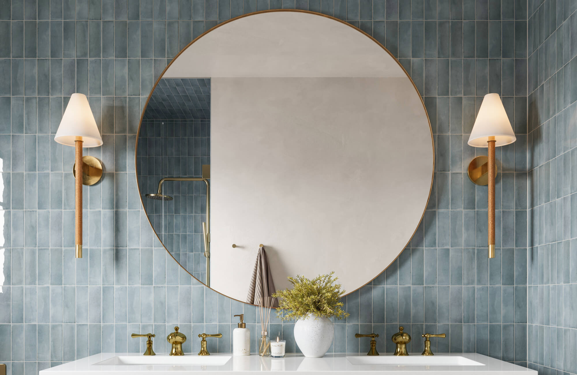 null Serene bathroom with handcrafted blue tiles, oversized round mirror, brass fixtures, and tapered sconces flanking a double vanity.