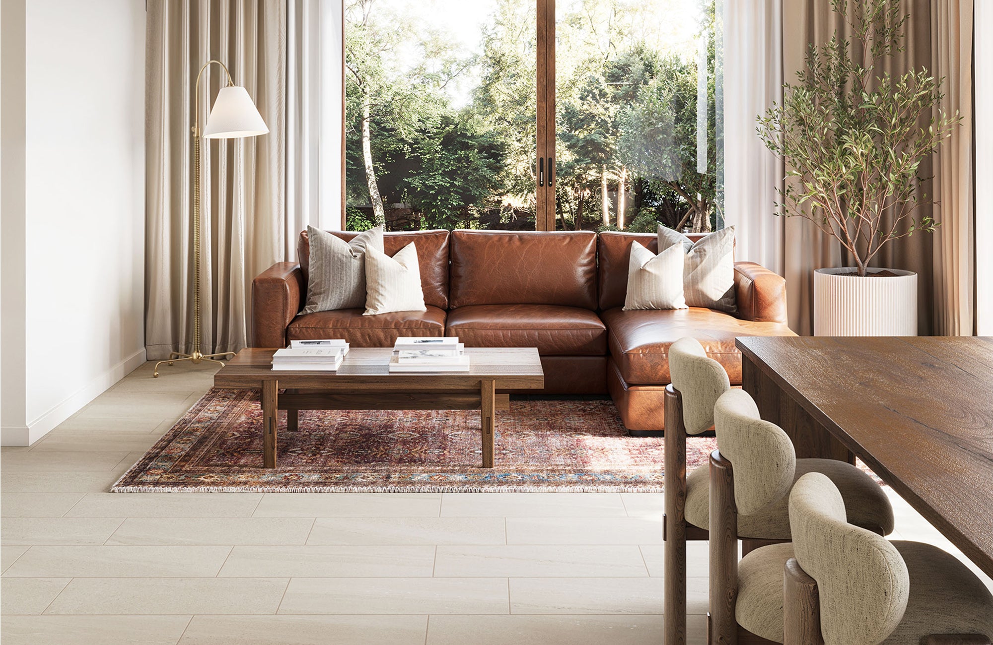 Rust-toned vintage rug adds warmth to a bright living room with a leather sectional, wood coffee table, and large window framing lush outdoor views.
