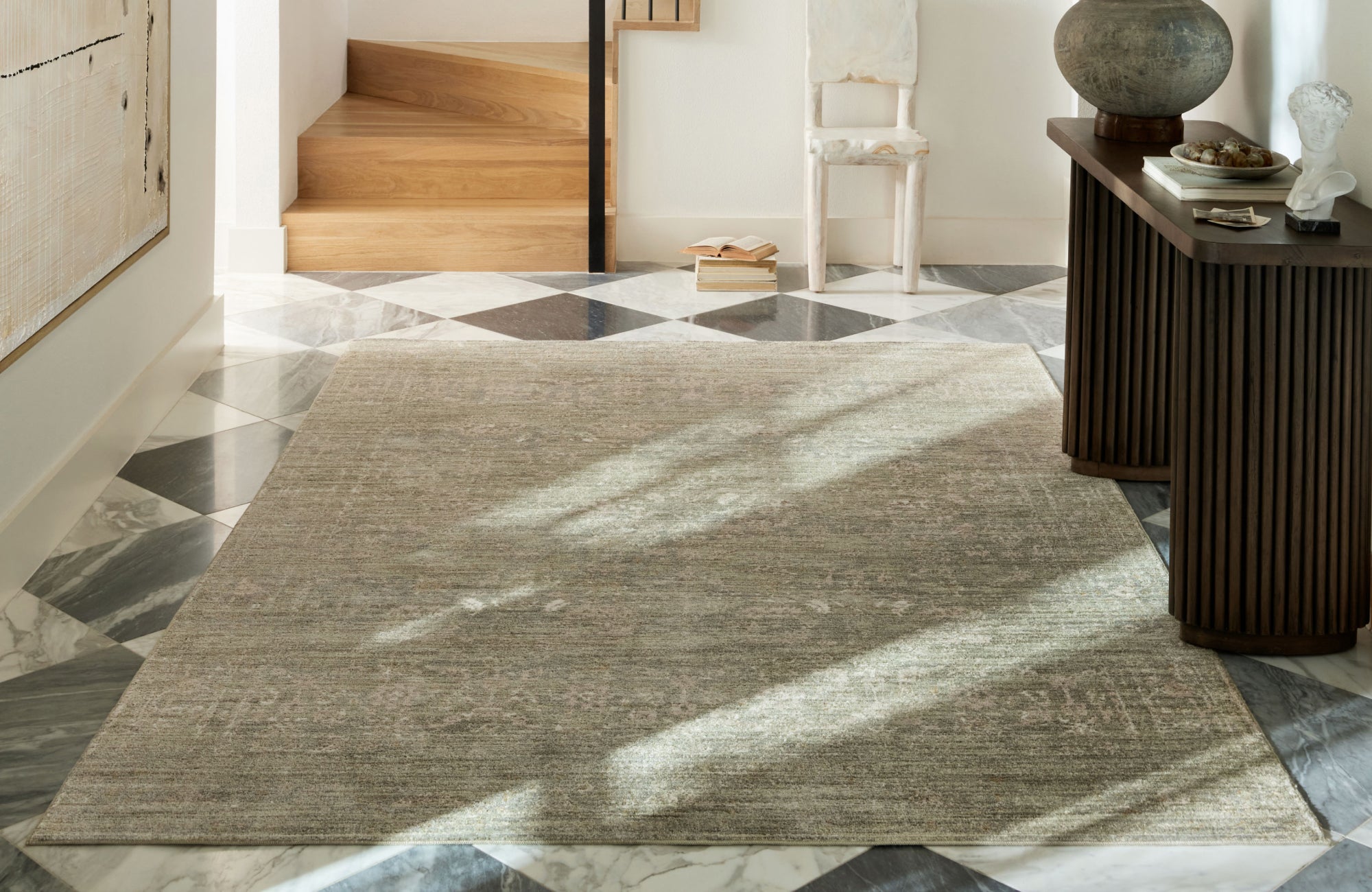 Textured gray area rug with organic linear patterns anchors a bright neutral-toned living room with a cream sofa, wood chair, and natural light.