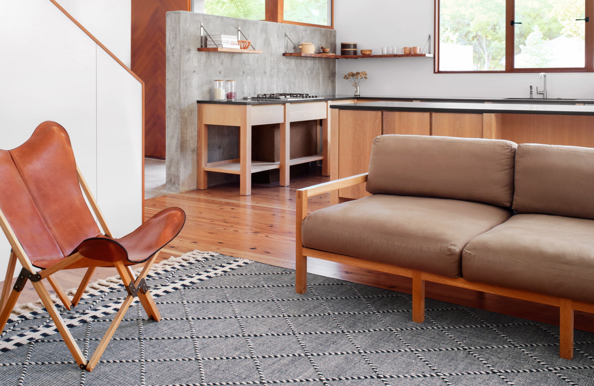 Modern open-plan room with leather chair and sofa, rug positioned lengthwise along furniture to support natural flow.