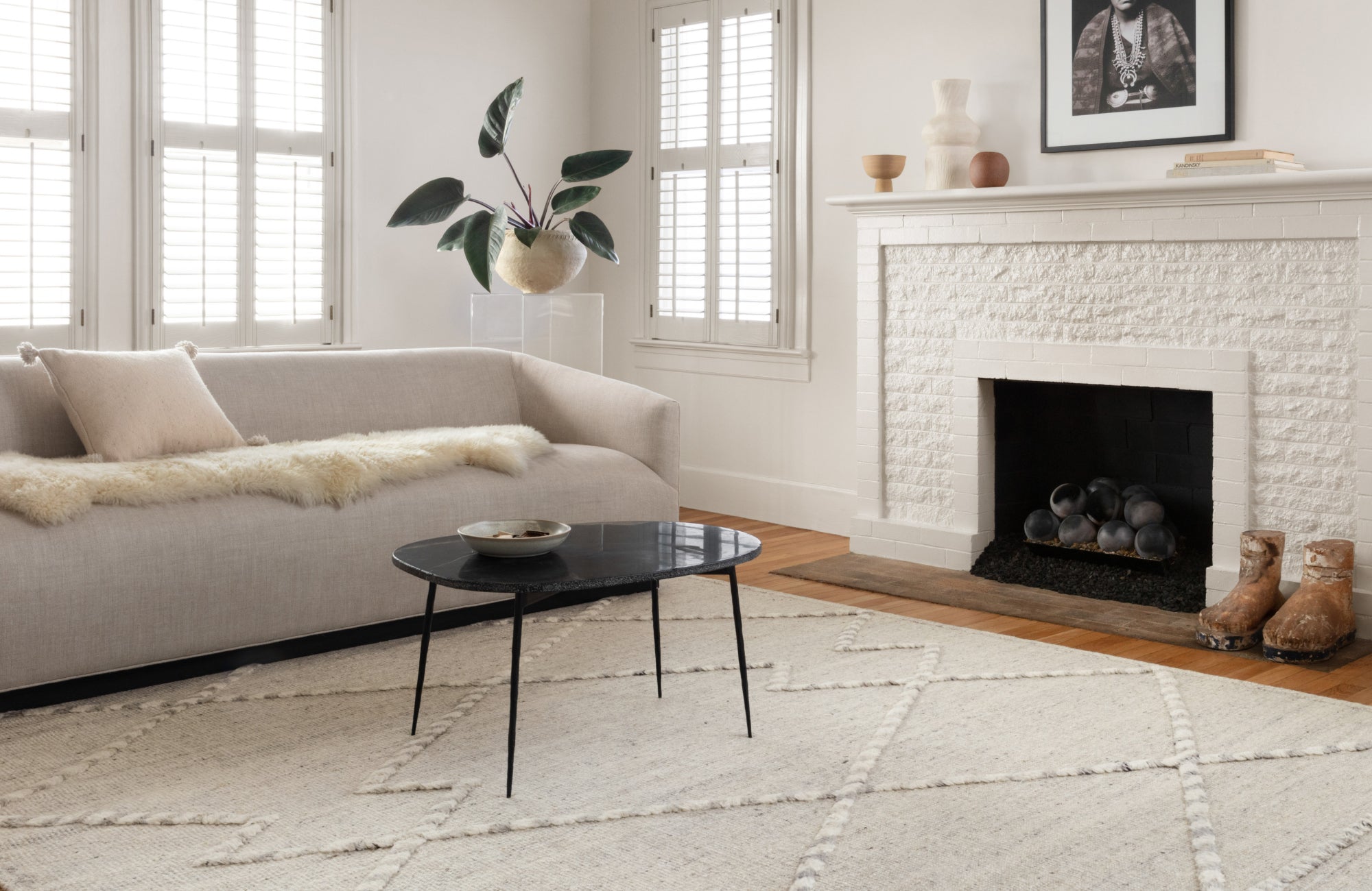 Neutral-toned room with fireplace and curved sofa, rug placed lengthwise to create depth and openness in the space.