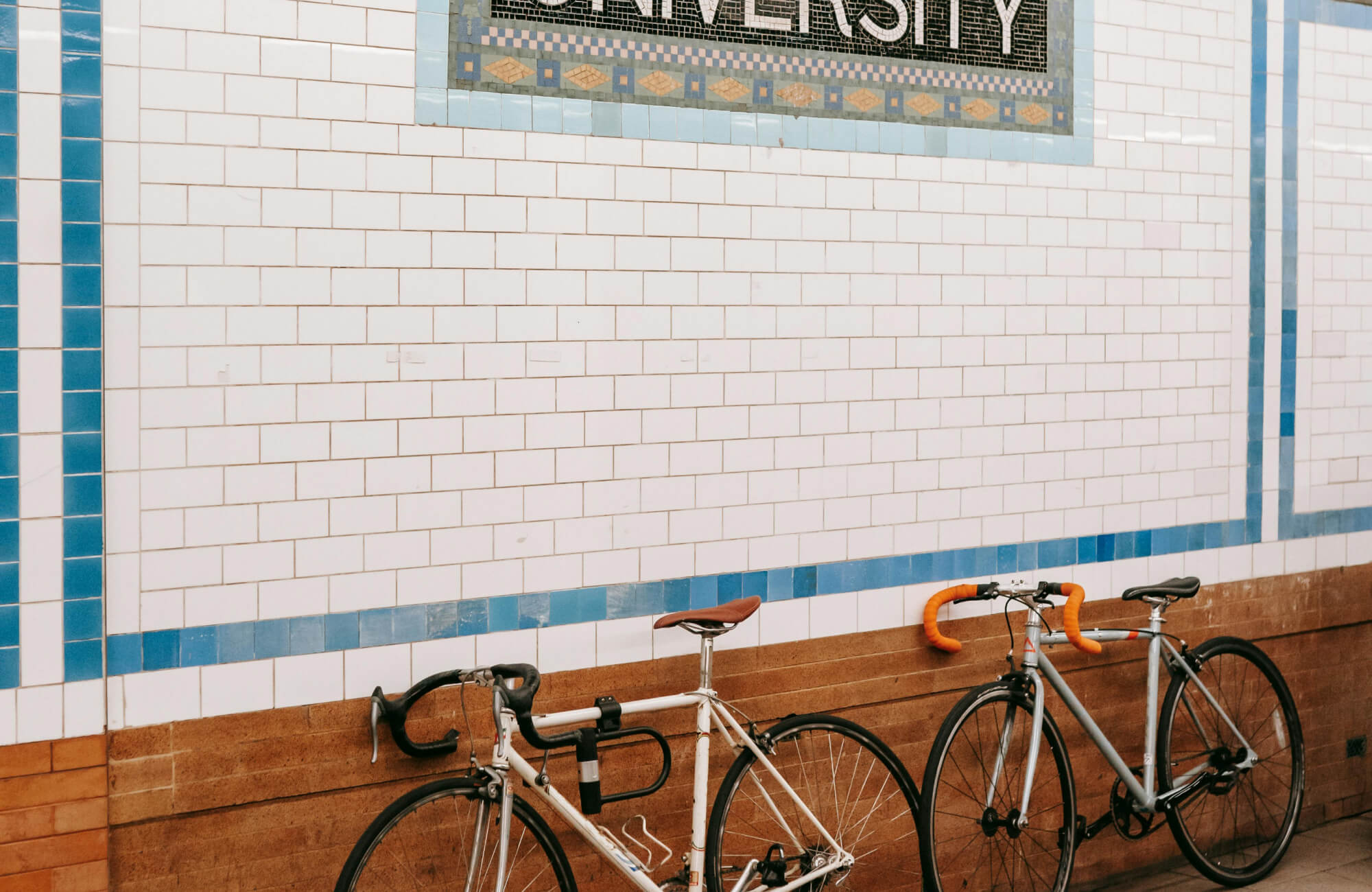 Classic white subway tile wall in public space with blue border, grout lines, and bicycles resting against tiled surface.