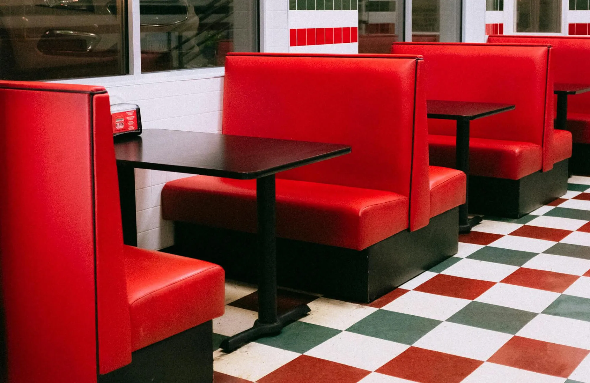 Classic American diner booth with red vinyl seats and retro checkered floor tiles, capturing the nostalgic design of mid-century diners.