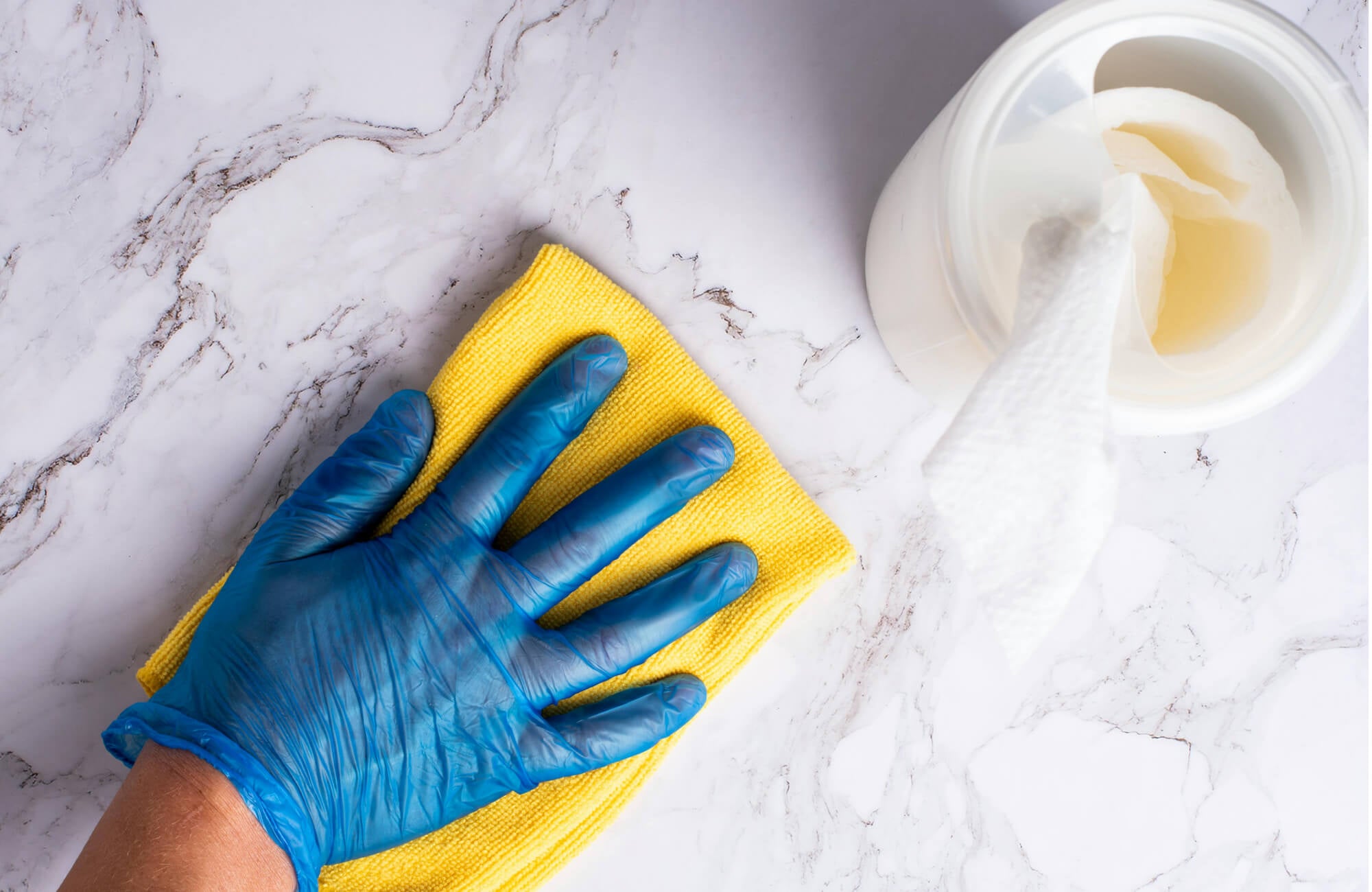 null Gloved hand cleaning polished marble surface with yellow cloth beside open container of cleaning solution.