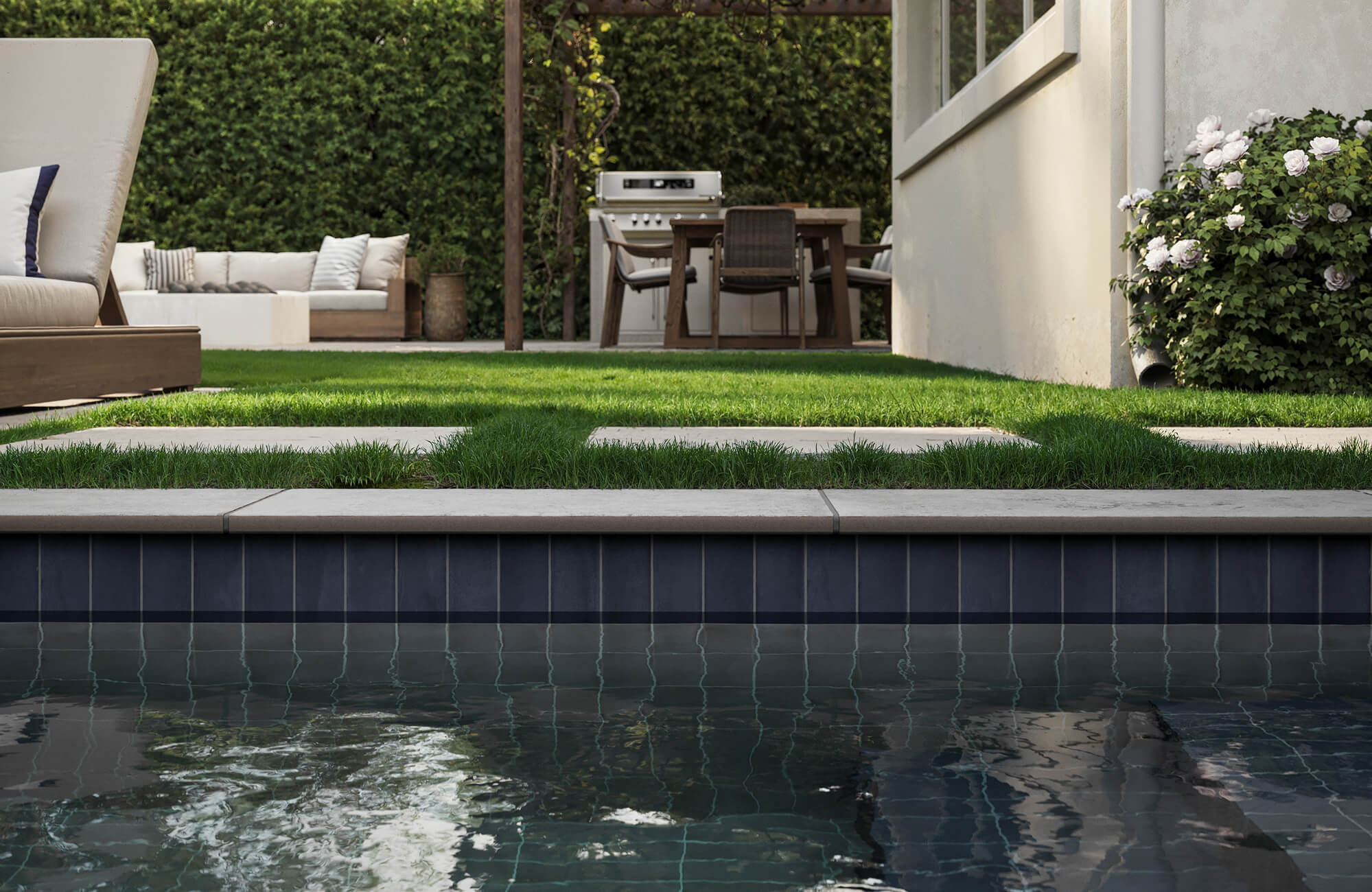 Sleek vertical pool tiles in deep navy add bold contrast to a lush garden and contemporary outdoor lounge.