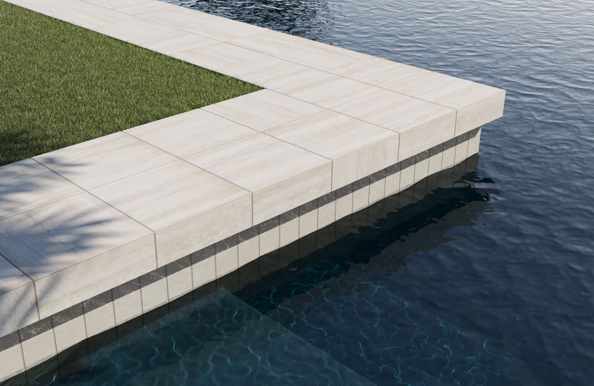 Beige stone-look pool tiles with a dark accent band create a clean, architectural edge beside vibrant green turf.