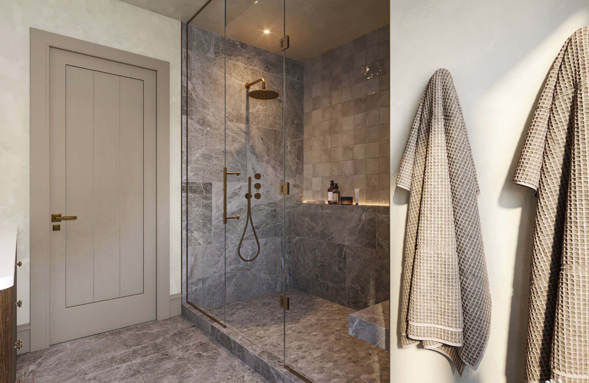 Elegant bathroom with a glass-enclosed shower, gray marble tiles, brass fixtures, and beige textured robes hanging on the wall.