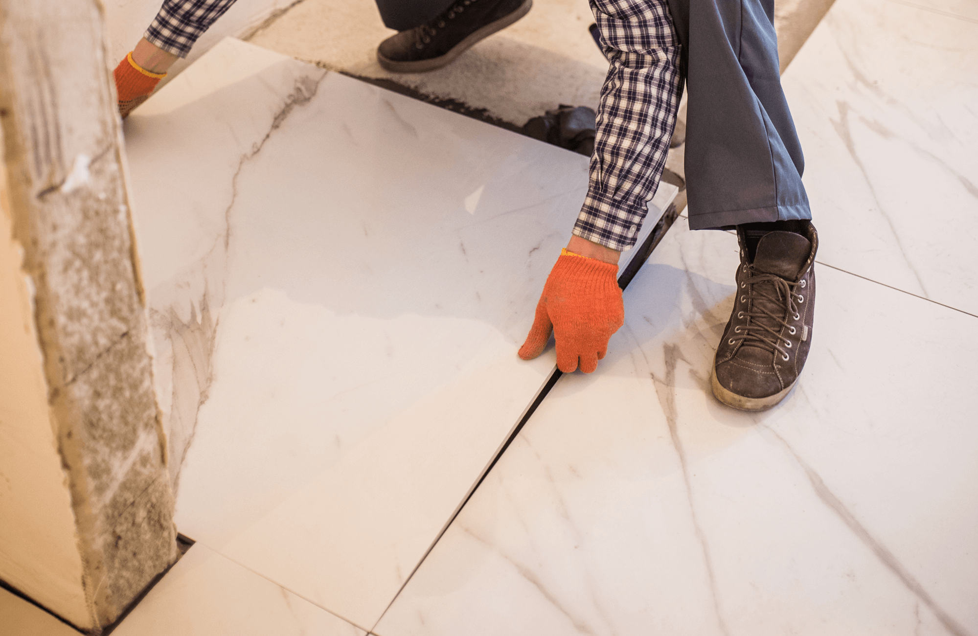 Worker in gloves installing large format marble tiles with subtle veining on a floor.