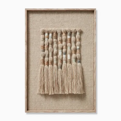 Framed textile wall art featuring hand-formed wool and jute knots arranged in vertical columns, with rounded, dimensional segments in soft earthy tones and long natural fringes that add movement and an organic, woven texture.
