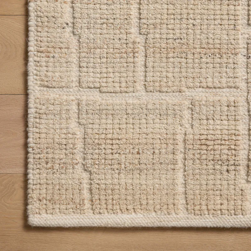 A close-up view of a warm beige wool-cotton blend rug, revealing a textured surface and subtle rectangular pattern created through a tightened, flattened weave.