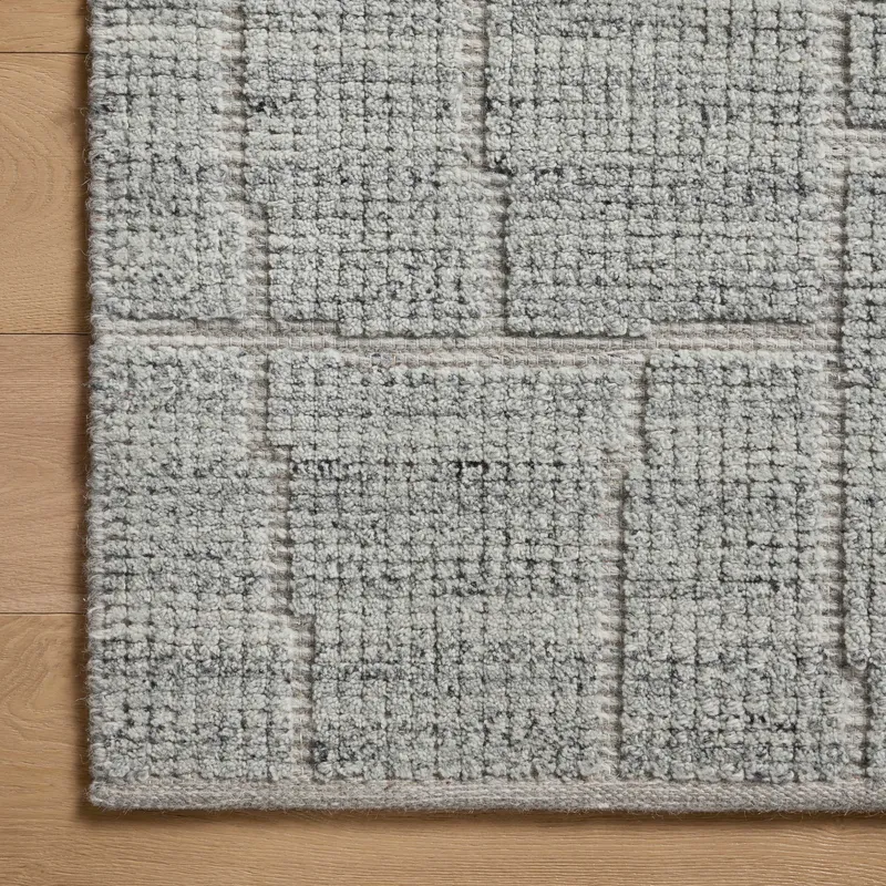 This detailed view highlights a bluish gray rug with subtle rectangular linework emerging from a flattened weave, revealing its hand-loomed, artisanal texture.