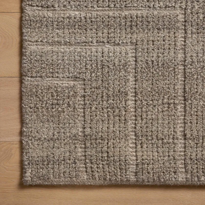 A close-up view of a brown rug with a dense, hand-loomed texture, showing subtle tonal shifts and angular lines that create a softly geometric pattern.