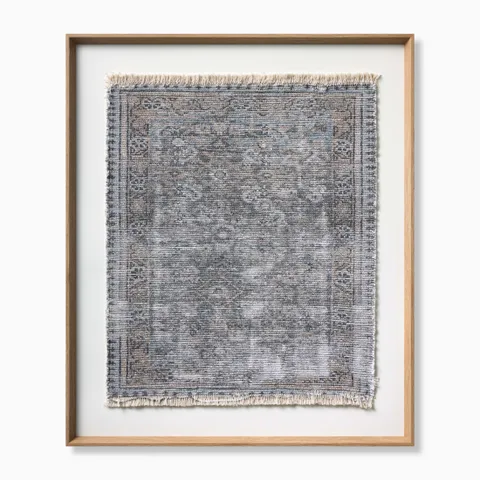 Framed textile wall art featuring a handwoven blue-gray rug panel with subtle traditional patterning, soft fringe edges, and a natural wood frame for a refined, artisanal look.