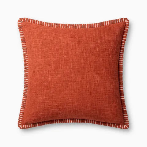 A warm dark orange pillow with woven texture, white whipstitched flange edges, and an antique bronze zipper concealed by a tailored flap, finished with a light, breathable cotton feel.