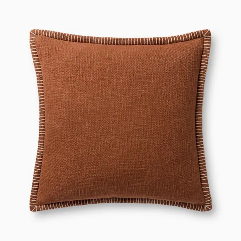 A warm reddish brown pillow with woven texture, white whipstitched flange edges, and an antique bronze zipper concealed by a tailored flap, finished with a light, breathable cotton feel.