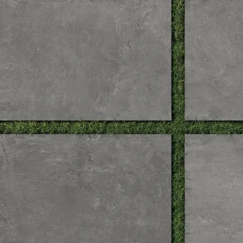 Close-up of Wren 24x36 grip porcelain 2cm paver tiles in charcoal, featuring a textured dark gray surface contrasted by lush green grass for sophisticated outdoor layouts.