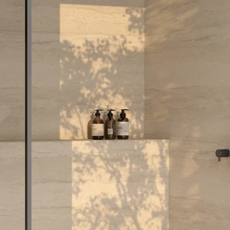 Warm beige tiled shower niche with soft sunlight and leafy shadows, highlighting a calm, natural spa-like moment.
