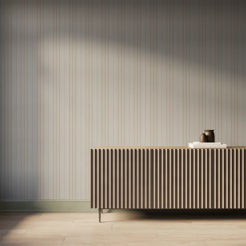 Warm tan vertical striped wallpaper behind a fluted wood sideboard with books and pottery, styled in a modern neutral interior.