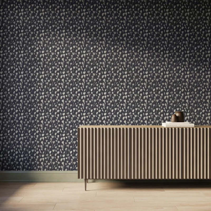 A wall with Petaline wallpaper Black II shows soft off-white floral silhouettes across a black background behind a fluted wood console, ideal for contemporary interiors.