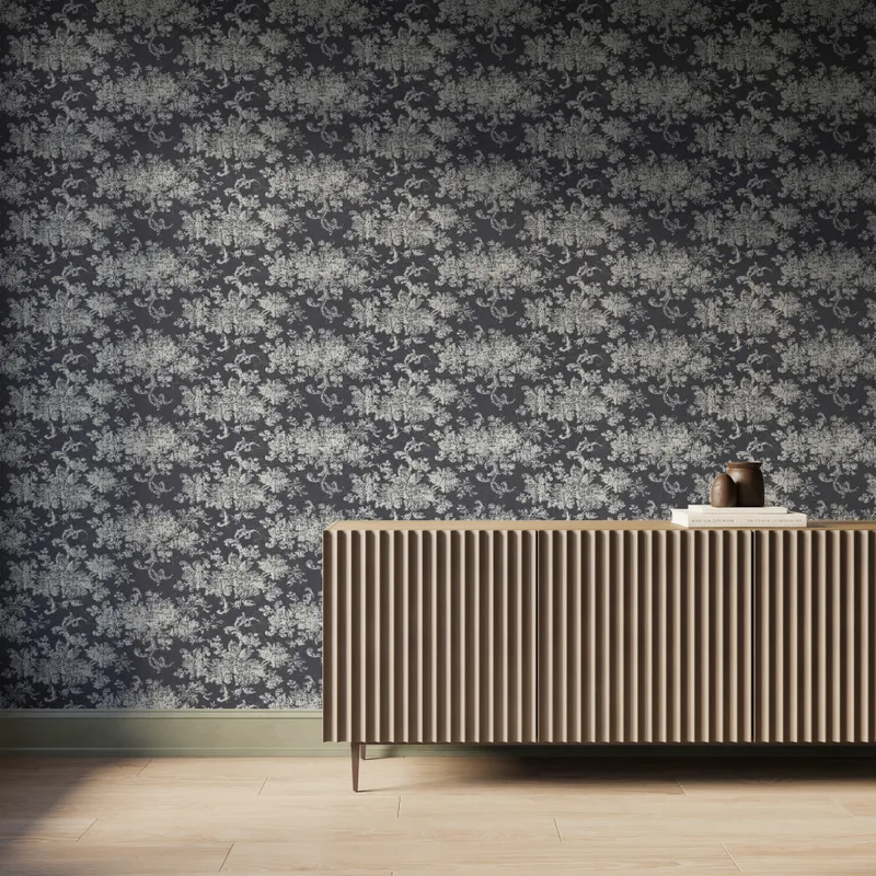 Interior scene featuring Brocade Wallpaper in Black I with a white damask floral motif over a matte black background, styled with a fluted wood console cabinet, decorative books and vases, and light wood flooring with soft natural light.