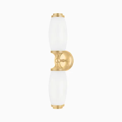 Our Cynthia Wall Sconce in Aged Brass blends smooth opal glass with curved symmetry, casting soft light through a rich, polished finish.