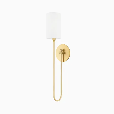 Foley wall sconce in aged brass with a graceful elongated arm and cylindrical white shade, offering refined illumination with modern charm.