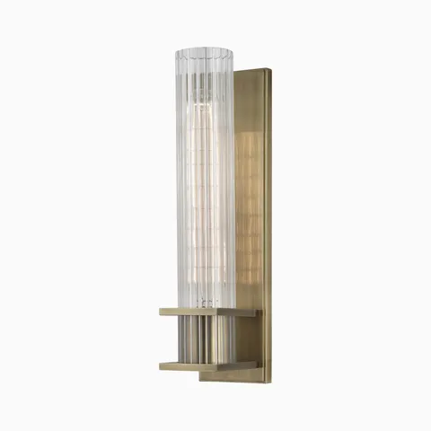Wall sconce with vertically grooved glass diffuser and cornered bands on a warm aged brass backplate, casting a softly textured glow.