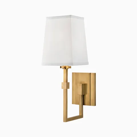 Aged brass wall sconce with tapered white fabric shade and geometric arm, creating a refined modern accent for bedrooms or hallways.
