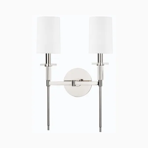 Polished nickel double wall sconce with two white cylindrical shades, slim vertical rods, and round backplate for a sleek modern accent.
