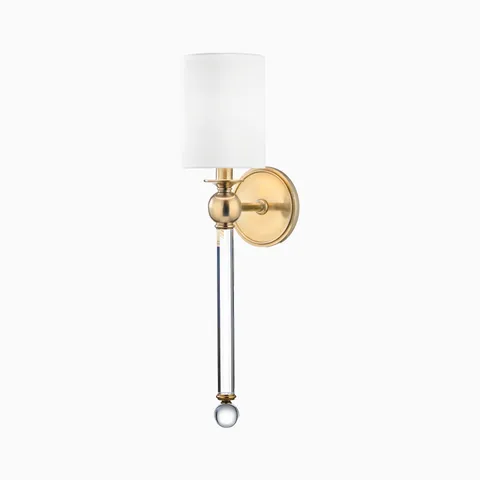 Aged brass wall sconce with white cylindrical shade, crystal rod accent, and round backplate, blending classic elegance with modern style.