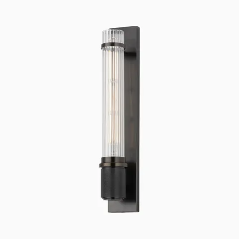 With a transparent fluted glass tube and near-black base, the Tyson Wall Sconce in Old Bronze delivers strong contrast and symmetry for moody, vintage-inspired spaces.