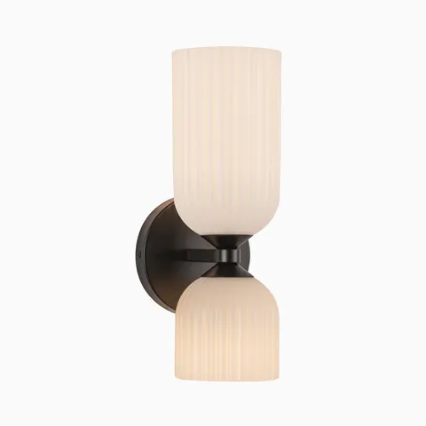 Modern wall light with a dark bronze backplate and dual ribbed glass shades arranged vertically, creating soft ambient lighting beside mirrors.