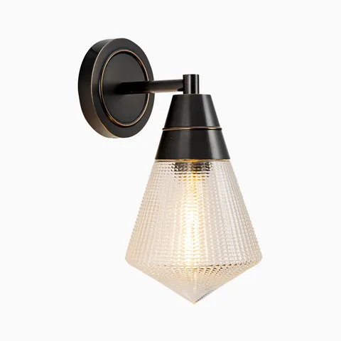 Matte black wall vanity light with a tapered metal socket and faceted clear textured glass shade mounted on a round backplate.